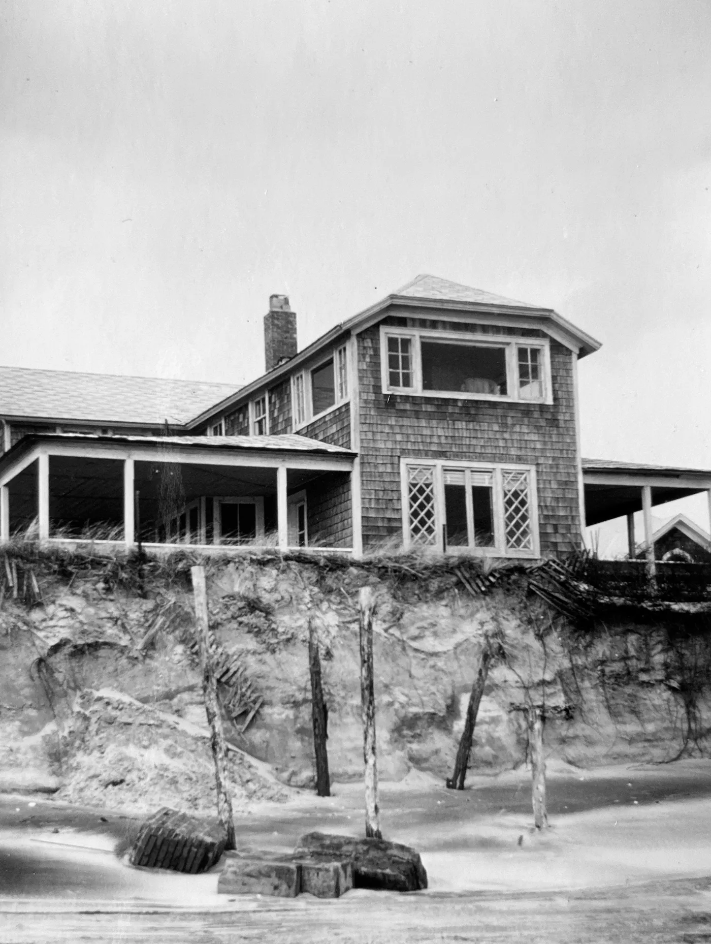 A shingled Fire Island house standing above an eroded dune, photographed in black and white